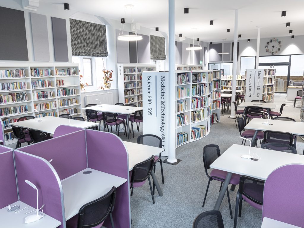 A white library with books on shelves desks and chairs.